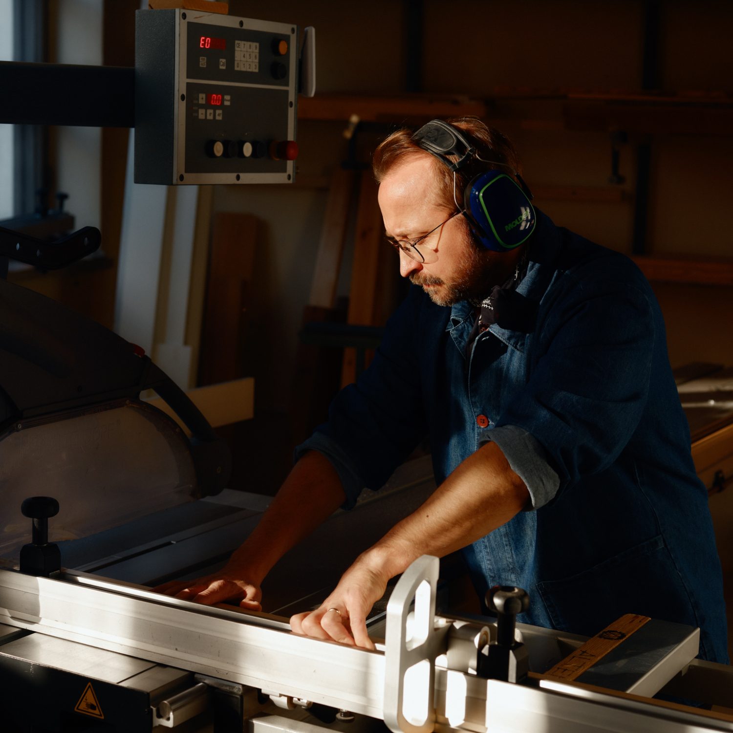 Person arbetar med träbearbetning vid en industrimaskin, iförd hörselskydd – typisk arbetsmiljö inom bygg- och hantverksbranschen.