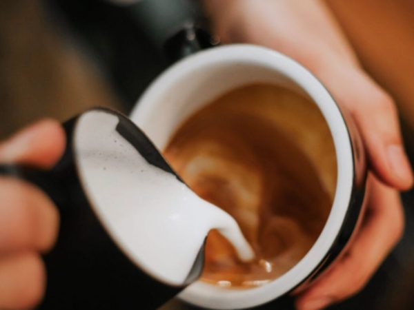 Närbild på händer som häller mjölkskum i en kopp kaffe för att göra en cappuccino eller latte.