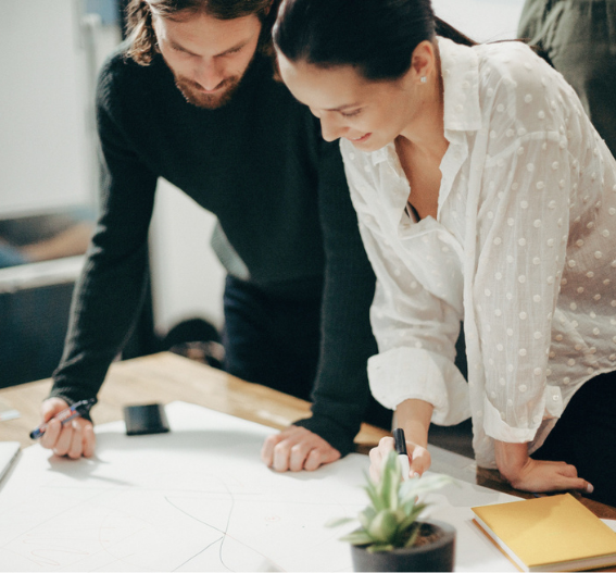 Två personer som samarbetar över ritningar vid arbetsbord, symboliserar helhetssyn, ekonomisk rådgivning och strategisk planering för företag.