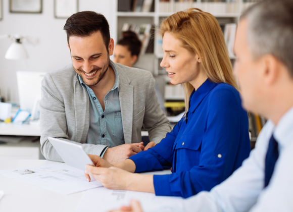 Tre personer i möte kring surfplatta, symboliserar samarbete, ekonomisk rådgivning och digitala arbetssätt inom redovisning och affärsutveckling.