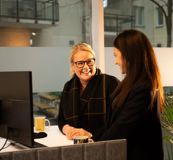 Två personer i samtal vid skrivbord på kontor, symboliserar personlig rådgivning, samarbete och stöd för företagets ekonomiska utveckling.